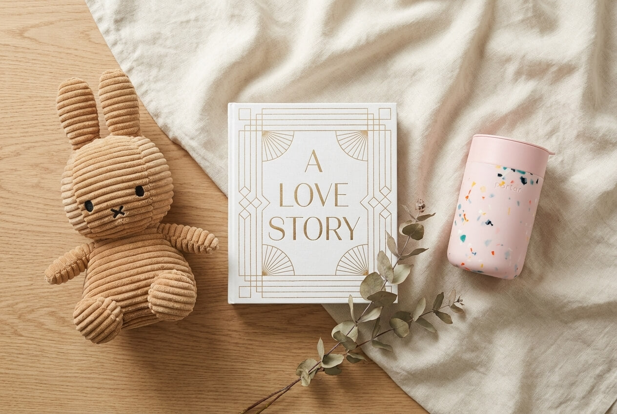 Plush rabbit toy, book titled 'A Love Story', and pink tumbler on a wooden surface with a white blanket.
