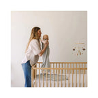 Woman holding a baby in a nursery with a crib and mobile.