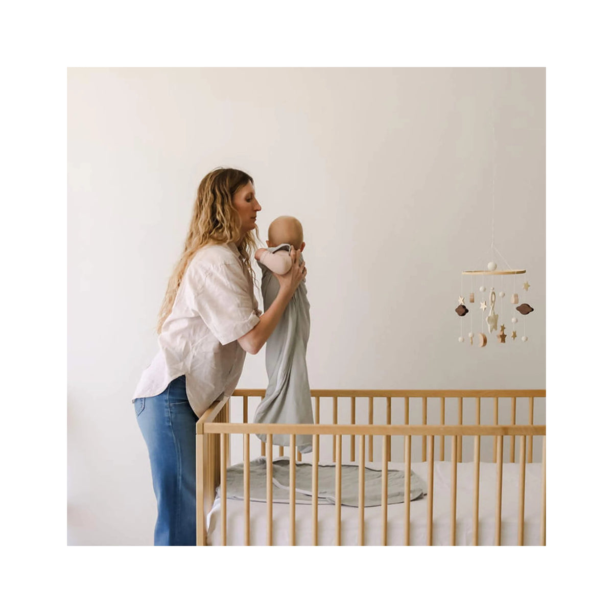 Woman holding a baby in a nursery with a crib and mobile.