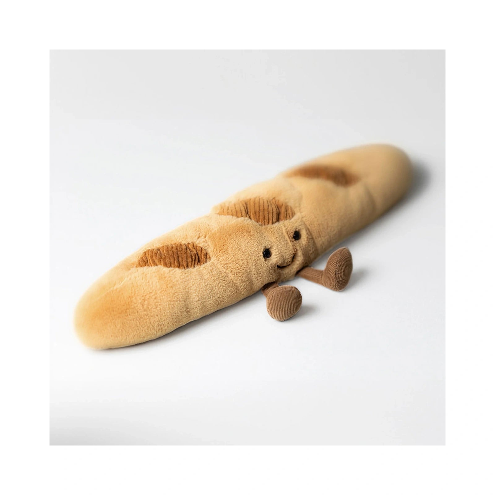 The Jellycat Amuseables Baguette plush toy features a golden brown soft fabric body with dark brown textured corduroy cuts, a cheerful embroidered face, and small corduroy legs resting on a clean white background.