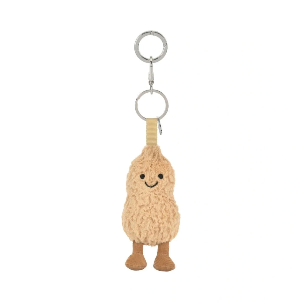 A plush peanut-shaped keychain charm with a smiling embroidered face, attached to silver metal key rings and a beige fabric loop, shown on a plain white background.