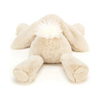 The back view of a beige Jellycat Smudge Rabbit Medium plush toy lying flat, featuring long floppy ears and a fluffy white tail.