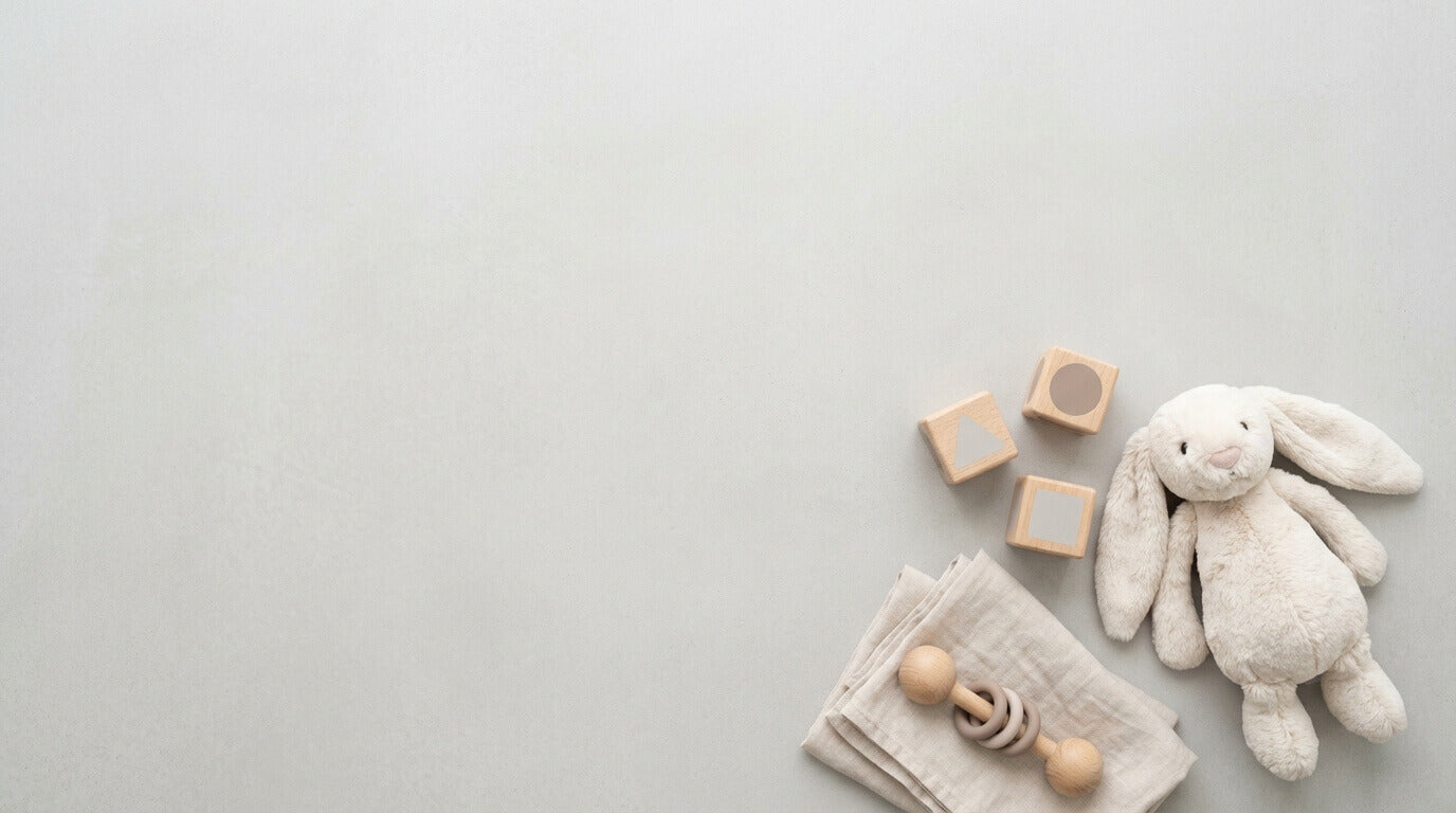 Baby toys including a plush bunny, wooden blocks, and a teething ring on a light gray background