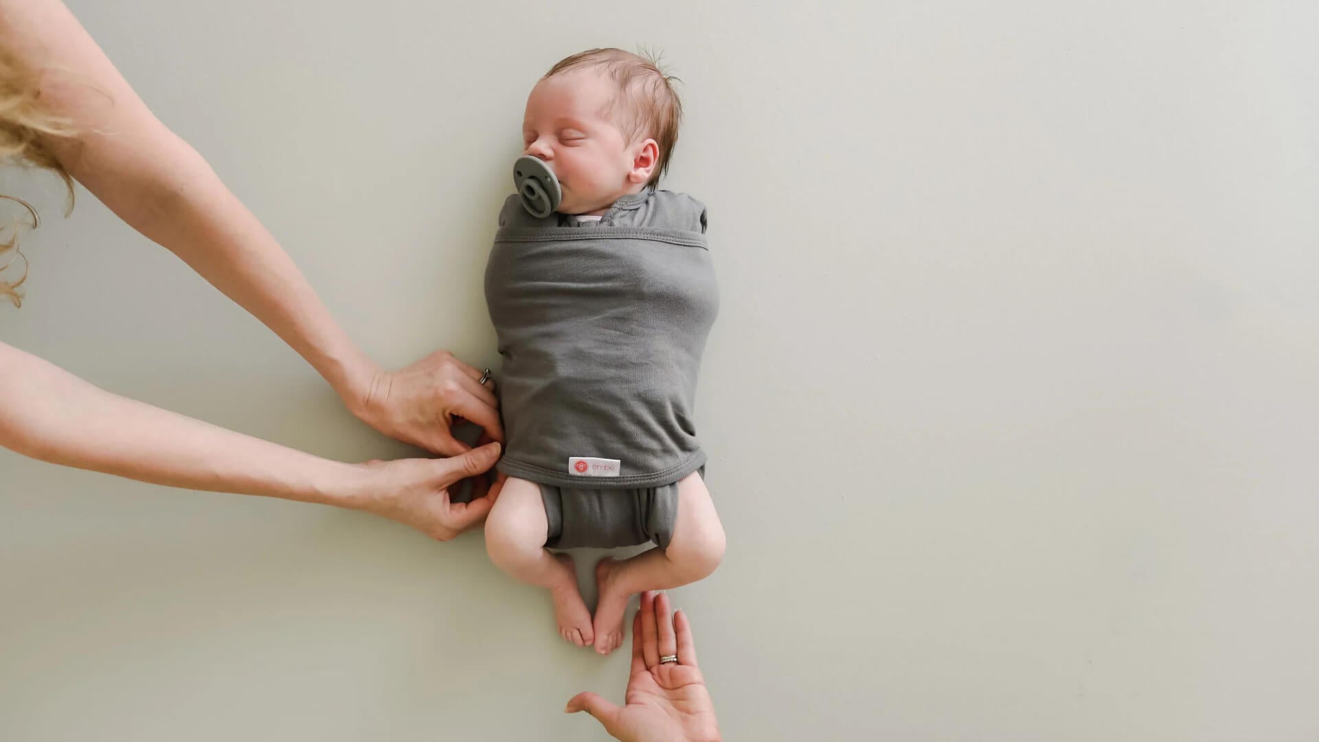 Newborn baby wrapped in a gray swaddle with a plain background