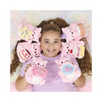 A young girl smiles while lying down surrounded by Pembe the Pink Cat soft toys, including the PEMBE BE YOU SMALL SOFT TOY and other themed pink plushies with colorful signs and cupcake designs.